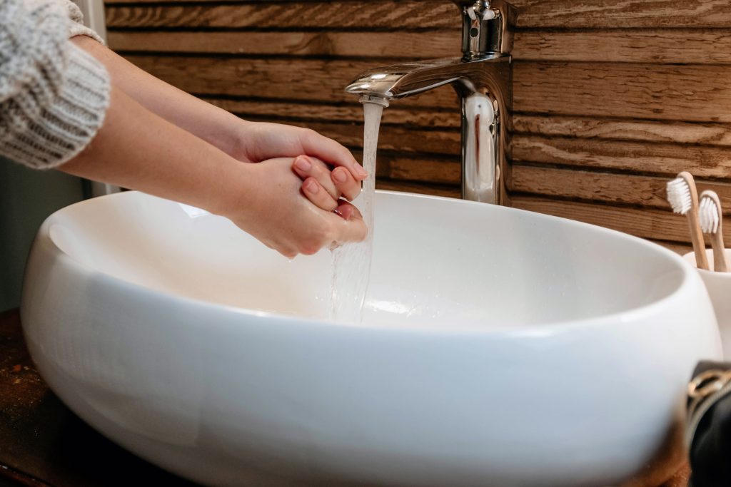 Nahaufnahme neutrale Farben Bild einer Frau, die sich die Hände über dem Waschbecken wäscht. Modernes Badezimmer mit weißem Waschbecken und Holzwand.