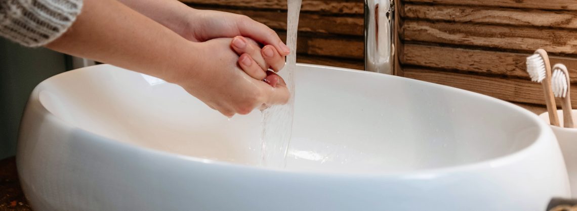 Nahaufnahme neutrale Farben Bild einer Frau, die sich die Hände über dem Waschbecken wäscht. Modernes Badezimmer mit weißem Waschbecken und Holzwand.