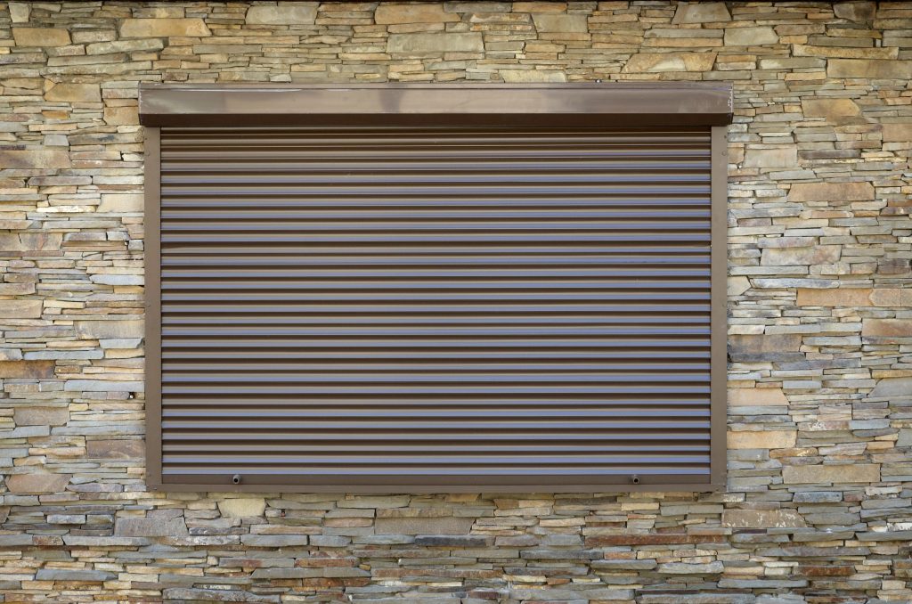 Aufsatz- oder Vorbaurollläden? 1 Ein Fenster mit braunen Vorbaurollläden aus Metall. Wanddekoration mit künstlichem Flachstein