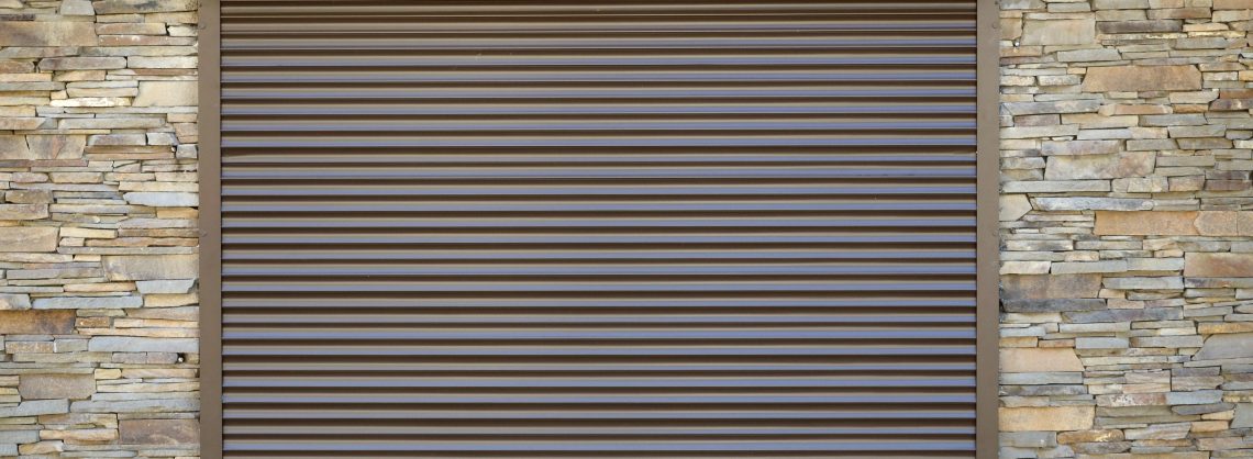 Ein Fenster mit braunen Vorbaurollläden aus Metall. Wanddekoration mit künstlichem Flachstein