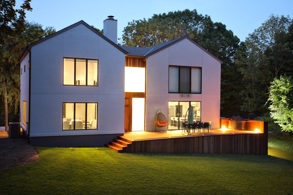 Ein Bild von einem modernen Luxushaus und Garten in der Dämmerung, das weiße Haus ist innen beleuchtet