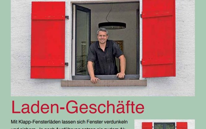 Auf dem Bild ist schaut ein dunkelhaariger Mann aus einem Fenster, an dem rote Holz-Fensterläden angebracht sind.