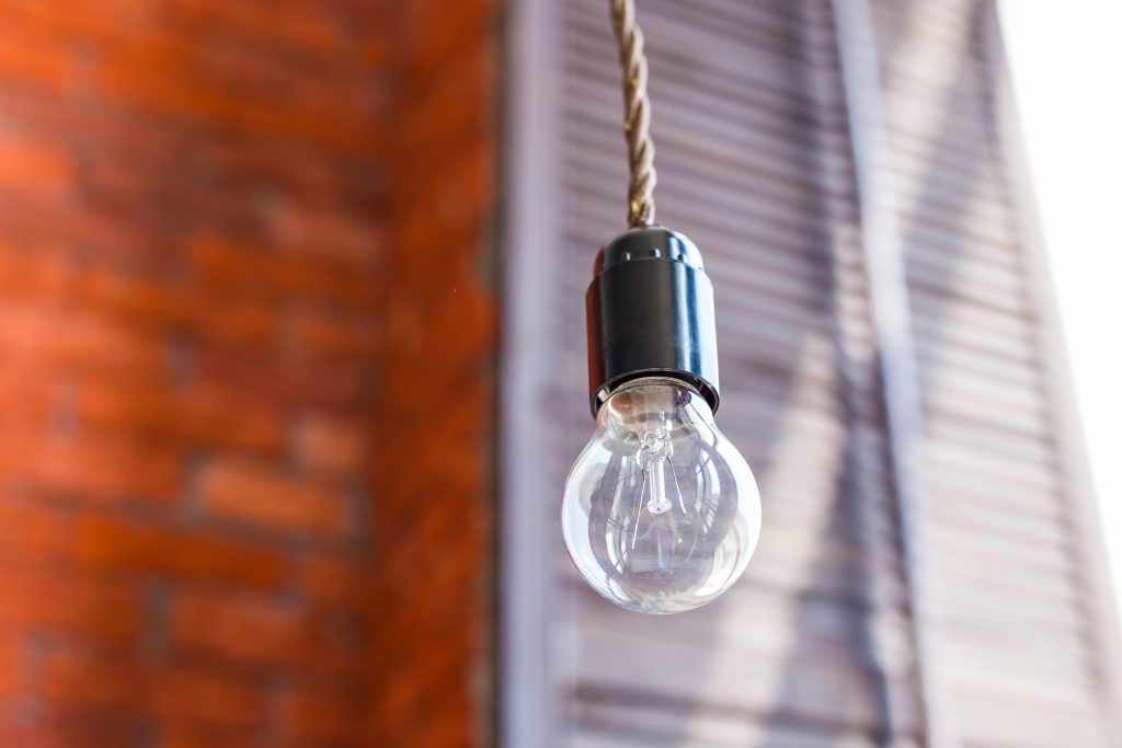 Stylische Lampenideen mit Textilkabeln 1 Glühlampe auf orangefarbenem Backsteinmauerhintergrund.