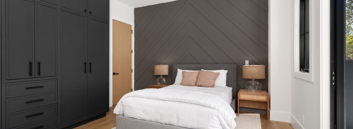 Modernes Schlafzimmer mit dunklen Einbauschränken, einem gemütlichen Bett und hölzernen Beistelltischen, einer Akzentwand mit Chevronmuster und Tageslicht.