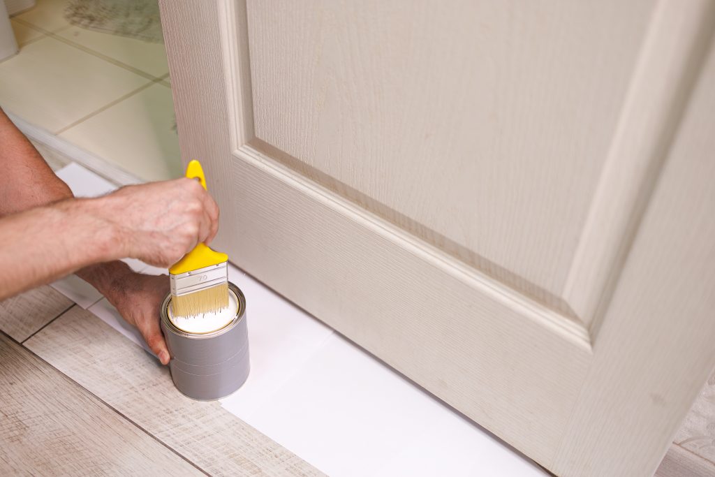Die einfache und günstige Renovierung von Innentüren 2 Die Hand, die den Pinsel hält, taucht ihn in die Farbe. Reparieren Sie die Flecken an den Türen mit Farbe