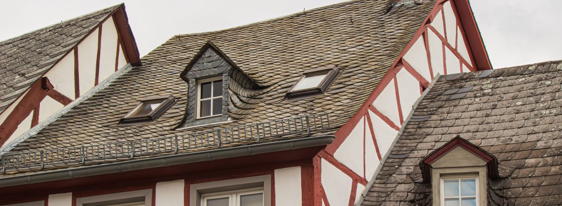 Ein weiß-rotes Fachwerkhaus mit grauem Dach und Gaube vor bewölktem Himmel.