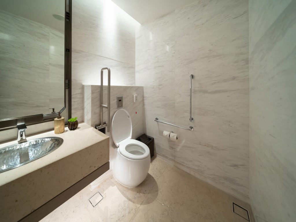 Aktuelle Trends für das Badezimmer 1 Barrierefreies modernes Badezimmer in beige, Toilette mit Hilfsgriffen und ein niedriges Waschbecken mit Spiegel.