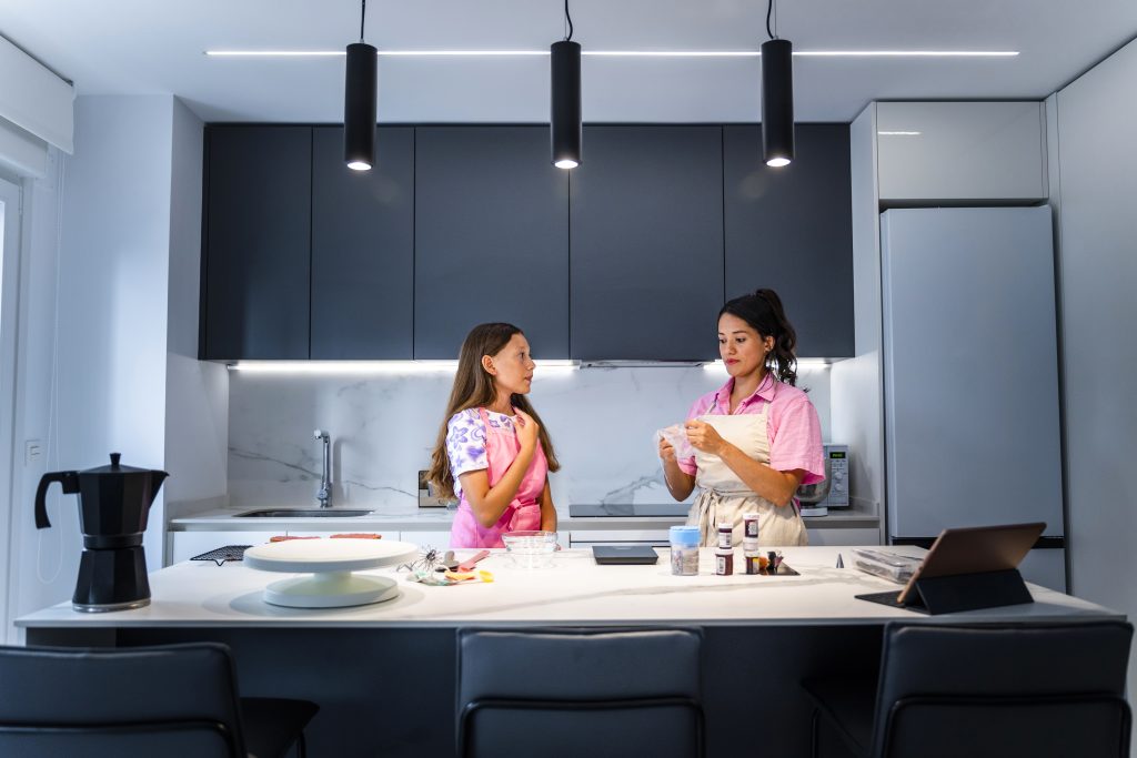 Modernisierung der Beleuchtung mit LEDS 1 Kochende Familie. Mutter und Tochter bereiten einen Spritzbeutel vor. Die Küche ist mit LEDs beleuchtet