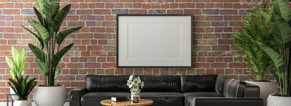 Industriell eingerichtetes Wohnzimmer mit roter Backsteinwand, grünen Zimmerpflanzen, einem dunkelgrauen Ecksofa und einem hellbraunen runden Holztisch auf einem weißen Teppich.