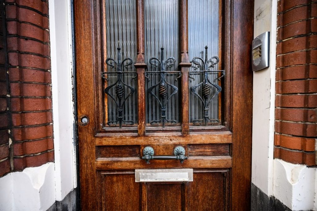Alte Haustür – lohnt sich die Renovierung? 1 Auf dem Bild ist eine alte braune Haustür mit Glasfenstern zu sehen, rechts und links sind Backsteinwände zu sehen.