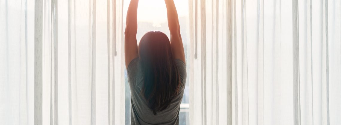 Junge asiatische Frau sitzt auf dem Bett und streckt sich morgens zu Hause