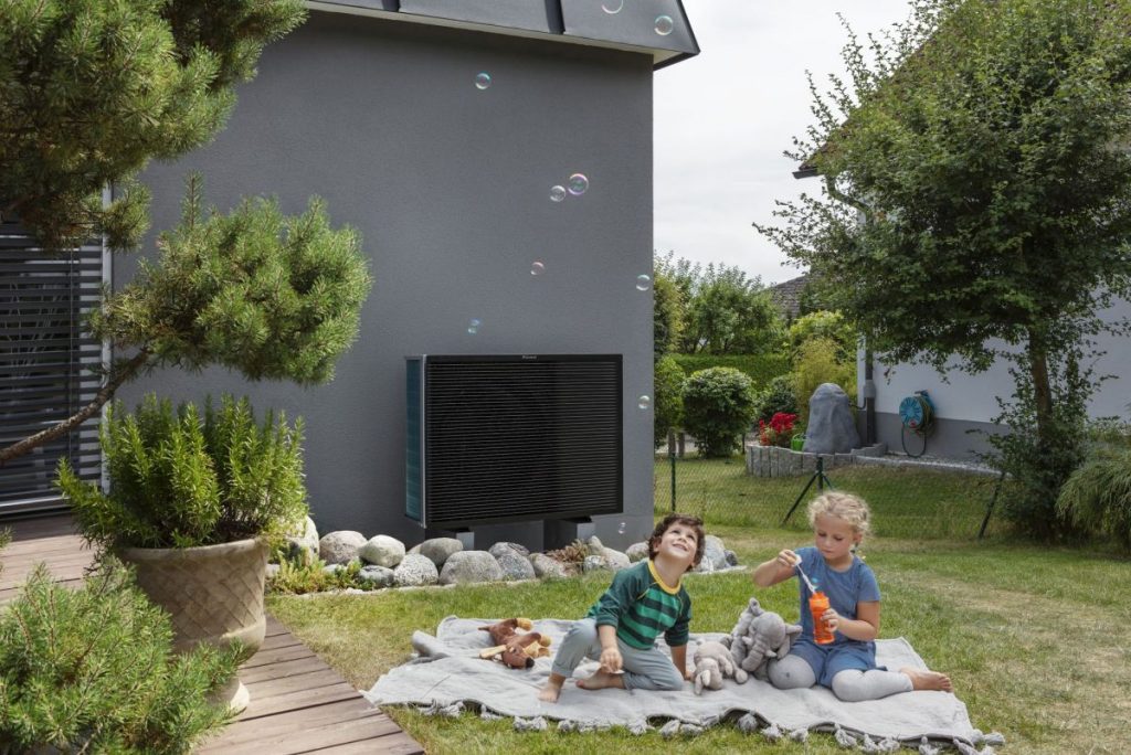 Kinder spielen mit Seifenblasen im Garten, im Hintergrund ist eine Wärmepumpe als Au0ßengerät sichtbar