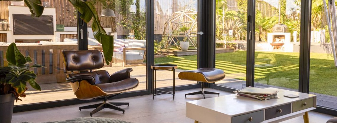 Zimmer mit Glaswänden und Blick auf Sitzgelegenheiten im Freien und Garten im modernen Haus