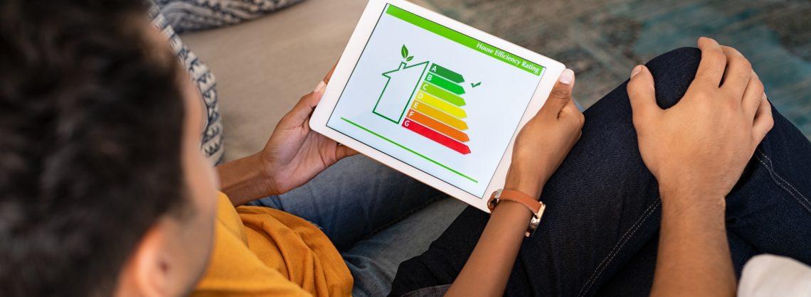 Ein POC Paar betrachtet auf einem Tablet die Energieklassen eines Hauses. Das Häkchen ist bei der dunkelgrünen Energieklasse A. Es gibt Energieklassen von A bis G, wobei A,B,C in verschiedenen Grüntönen gehalten ist, D und E in gelb und orange und F und G in zwei Rottönen.
