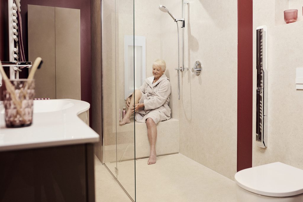 Eine Seniorin sitzt entspannt in einer modernen, barrierefreien Dusche mit gemauerter Sitzbank.